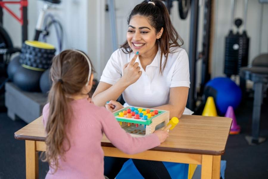 Terapeuta em reforço positivo com menina autista durante a terapia ABA.
