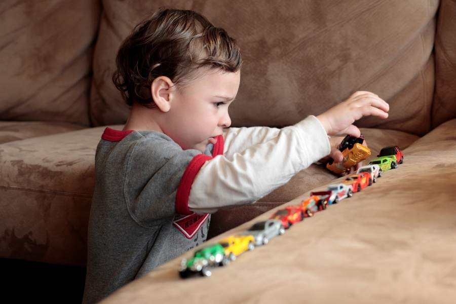 Menino autista brincando sozinho enfileirando carrinhos de brinquedo.
