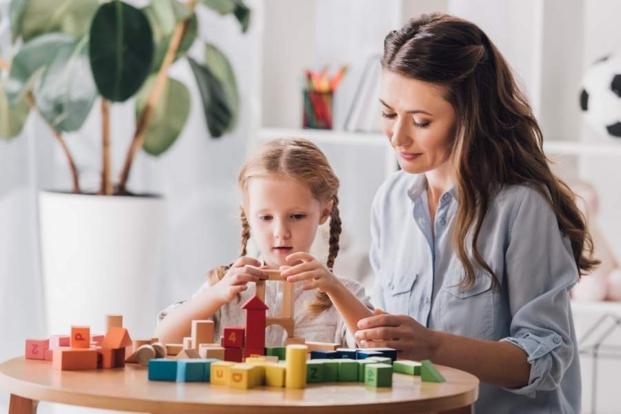 Menina autista brincando com blocos e com o suporte de sua mãe. 