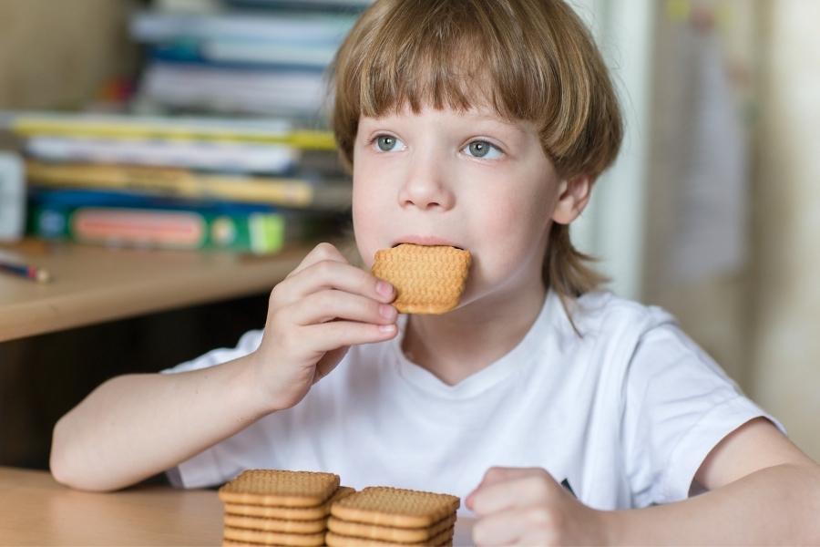 Menino autista comendo fiscoitos enfileirados representando a rigidez cognitiva em comer o mesmo lanche todos os dias.